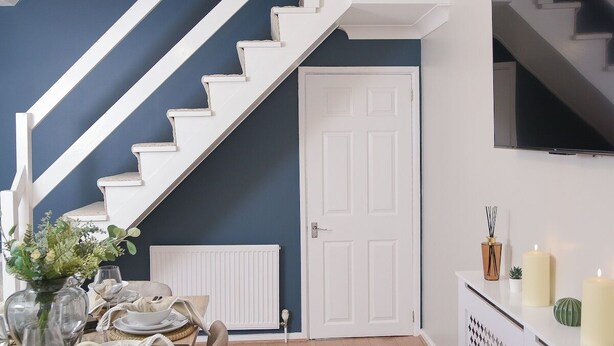 A dining area with a wooden table set for four, a white staircase, and a white door. - Stylish 3-Bed • Hot Tub • Free Parking • Contractors (Essex)