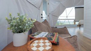 A cozy reading nook with a potted plant, a wooden chessboard, and books on a table. - The Dome At The Ridge-A Glamping Experience On The Bourbon Trail (Raywick)