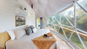 A bedroom with a large window, a bed with pillows, a framed picture on the wall, and a view of the outdoors. - The Dome At The Ridge-A Glamping Experience On The Bourbon Trail (Raywick)