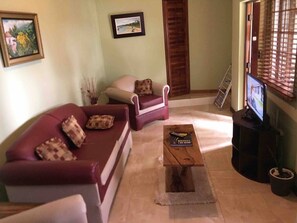 A living room with a red sofa, a matching armchair, a wooden coffee table, and a television on a stand.