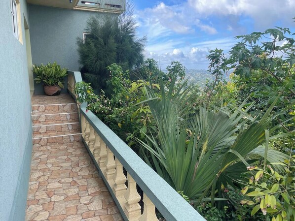A stone staircase leading to a balcony with a view of lush greenery and a distant landscape.