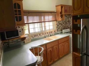 A kitchen with wooden cabinets, a stainless steel refrigerator, and a window with blinds.