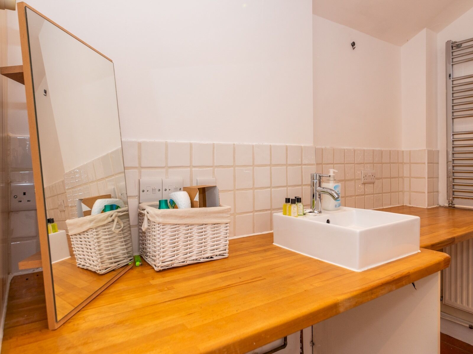A bathroom with a wooden countertop, a white sink, a mirror, two wicker baskets, and a towel rack.
