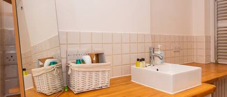 A bathroom with a wooden countertop, a white sink, a mirror, two wicker baskets, and a towel rack.
