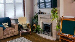 A living room with a fireplace, a sofa, a chair, and a television mounted above the fireplace. - Cosy Home w/ Stylish Interior – PassTheKeys (Watford)