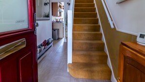 A staircase with a carpeted finish leading to a second floor. A red door with a glass panel is visible on the left, and a small wooden cabinet is on the right. - Cosy Home w/ Stylish Interior – PassTheKeys (Watford)