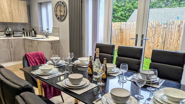 Área de refeições com mesa posta para quatro, cozinha ao fundo e vista para o exterior.