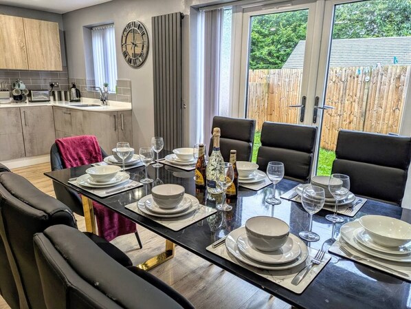 A dining area with a table set for four, kitchen in the background, and a view of the outdoors.