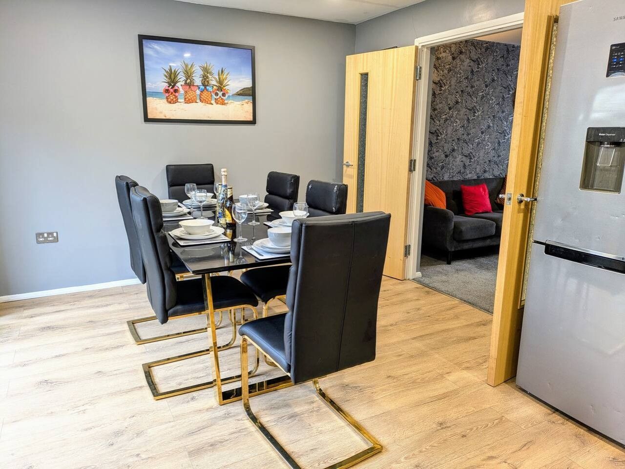 A dining area with a table set for four, a refrigerator, and a sofa in the background.