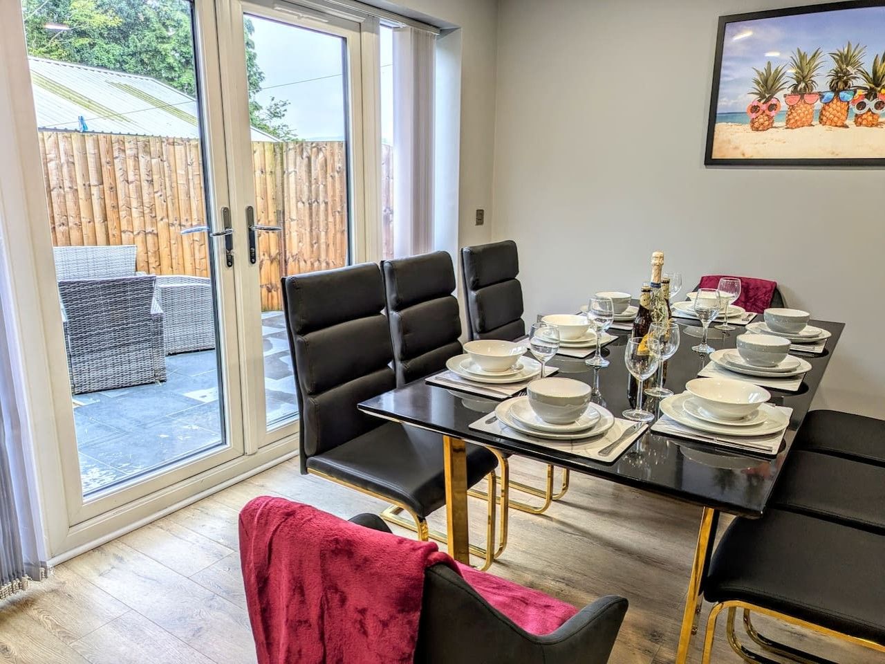 Comedor con mesa de vidrio preparada para cuatro, sillas tapizadas de color negro y vista a una valla de bambú a través de un puerta corrediza de vidrio.