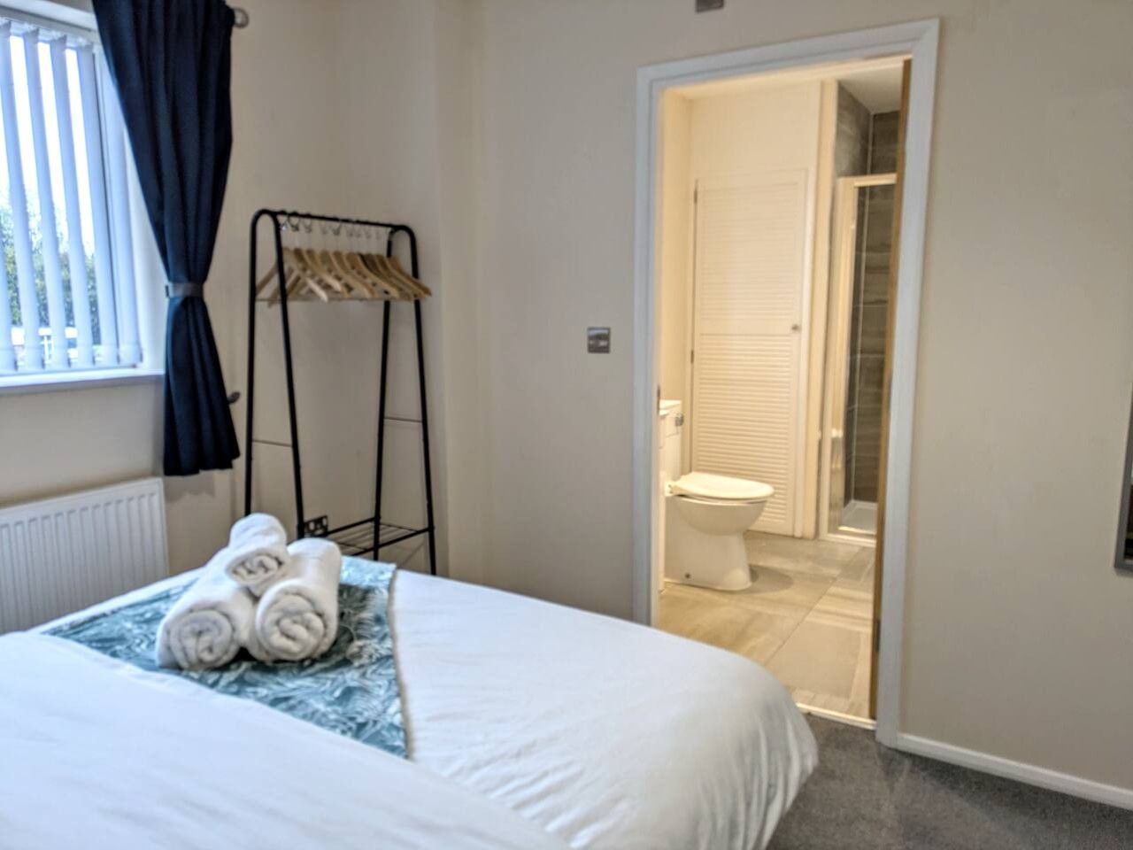 Une chambre d’hôtel avec un lit, une fenêtre avec des rideaux, un porte-serviettes et une porte donnant accès à une salle de bain.
