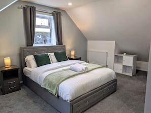 A bedroom with a bed, nightstands, a radiator, and a window with curtains.