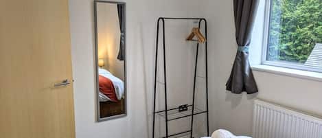A hotel room with a bed, a mirror, a radiator, a window with curtains, and a towel rack.