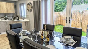 Uma área de refeições com mesa de vidro, cadeiras pretas e uma garrafa de champanhe.