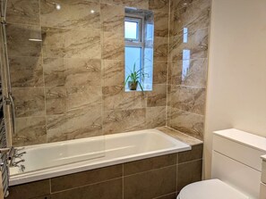 A bathroom with a bathtub, a window, and a toilet.
