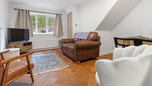A modern living room with a brown leather sofa, a white armchair, a wooden coffee table, and a television on a wooden stand. - Beautiful Renovated Central Home in York with Free Parking | Pass The Keys (York)