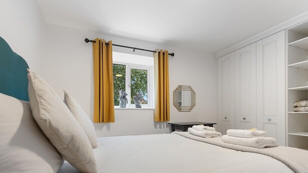 A bedroom with a bed, a window with curtains, a bedside table with towels, a mirror, and a wardrobe. - Beautiful Renovated Central Home in York with Free Parking | Pass The Keys (York)