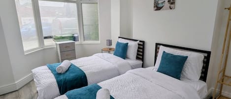 A hotel room with two beds, a window with blinds, a small table with a lamp, and a picture on the wall.