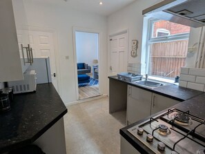 A compact kitchen with a gas stove, a sink, and a window overlooking a wooden fence.