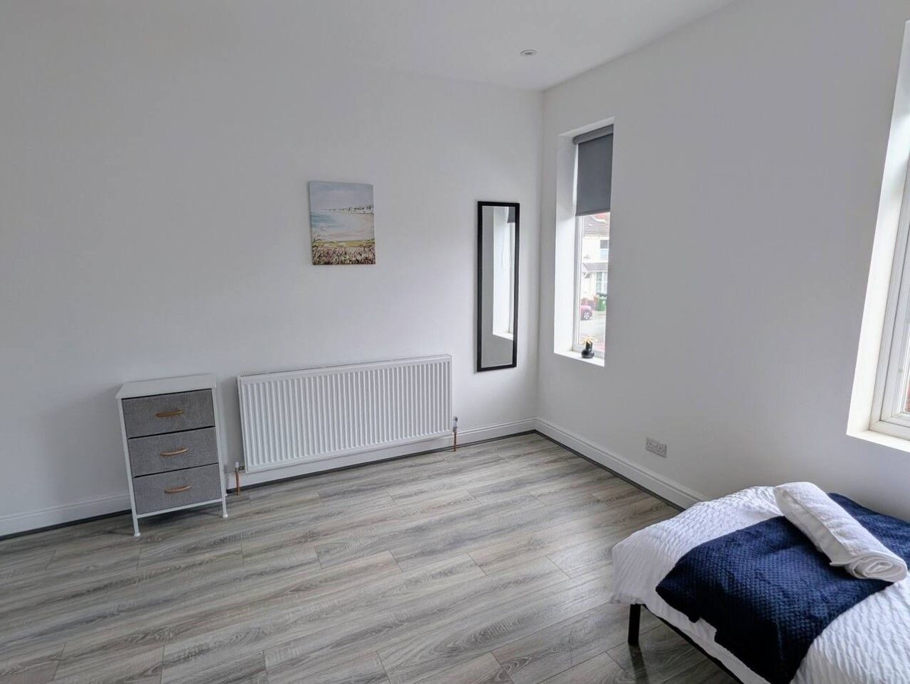 Ein Schlafzimmer mit einem Bett, einem Heizkörper, einem Fenster und einem an der Wand hängenden Bild.
