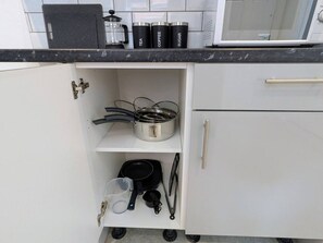 Een keuken met witte kasten, een zwart aanrecht en een magnetron. Er staan drie zwarte bakjes met de labels thee, koffie en suiker.