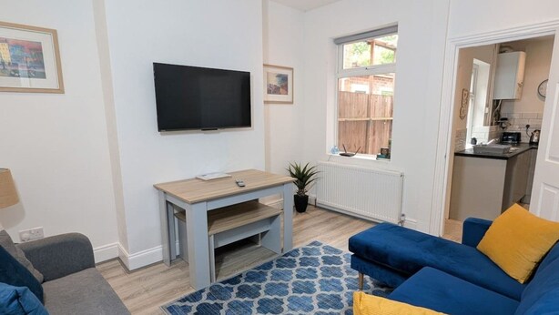 A living room with a flat-screen TV, a blue sofa, a grey sofa, a small wooden table, and a patterned rug. - Contractors 4BR Home, Newly Refurb, Nr Centre (West Midlands)