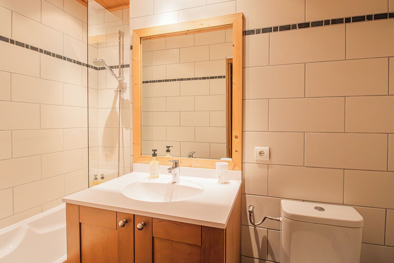 A bathroom with a white sink, wooden cabinets, a mirror, a shower, and a toilet.