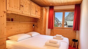 Habitación de cabaña de madera con una cama, dos almohadas, una mesita de noche y una ventana con cortinas rojas.