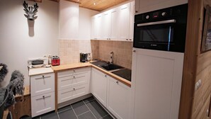 Cocina compacta con armarios blancos, horno Bosch y techo de madera.