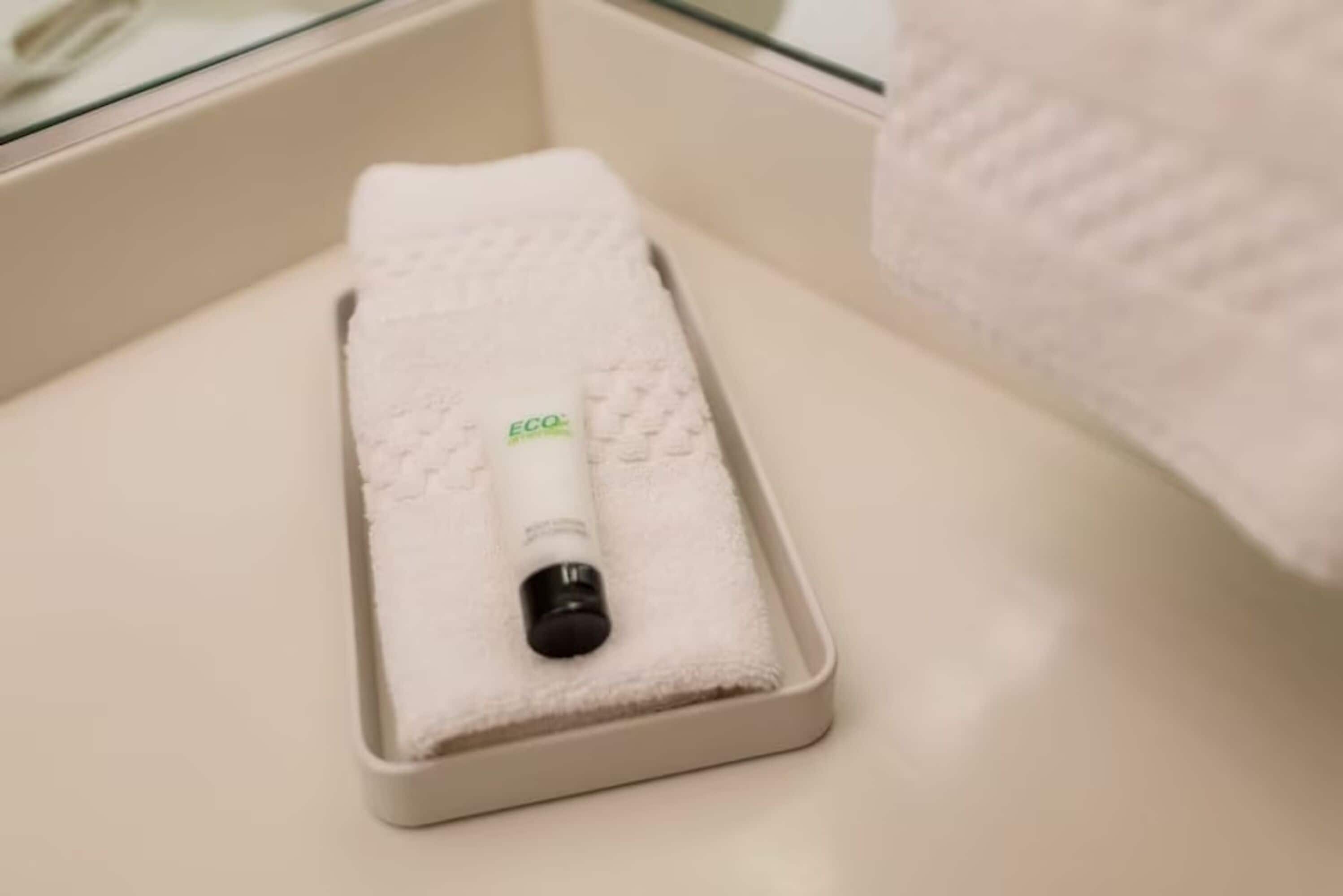 A white bathroom with a glass shower enclosure, a white towel, and a bottle of ECO soap.