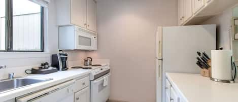Una cocina moderna con armarios blancos, microondas integrado, estufa y refrigerador.