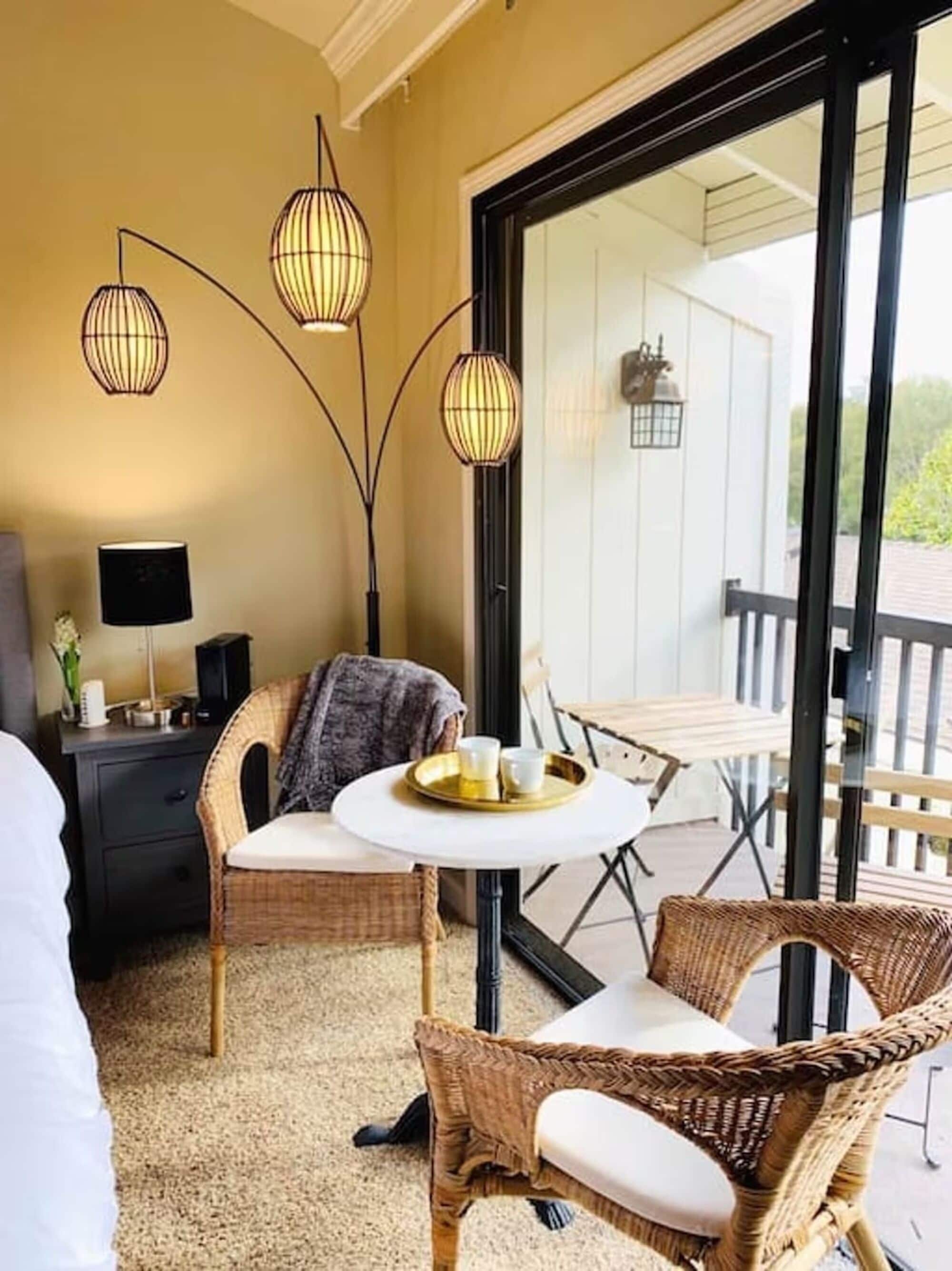 Habitación con mobiliario de mimbre, una mesa redonda con bandeja y un amplio ventanal corredero que da a un espacio exterior.