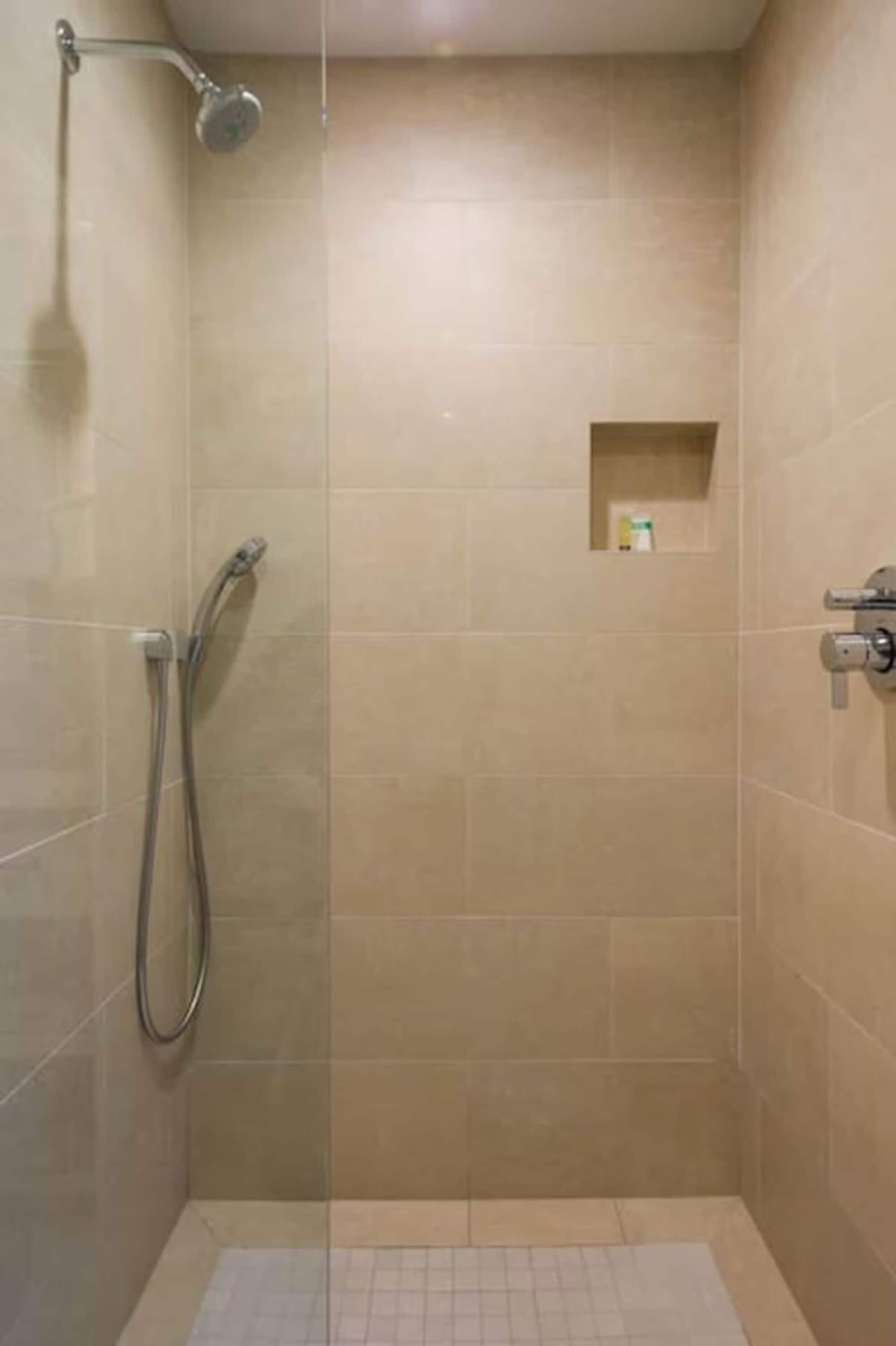 A small, enclosed shower area with beige tiles, a handheld showerhead, and a wall-mounted faucet.