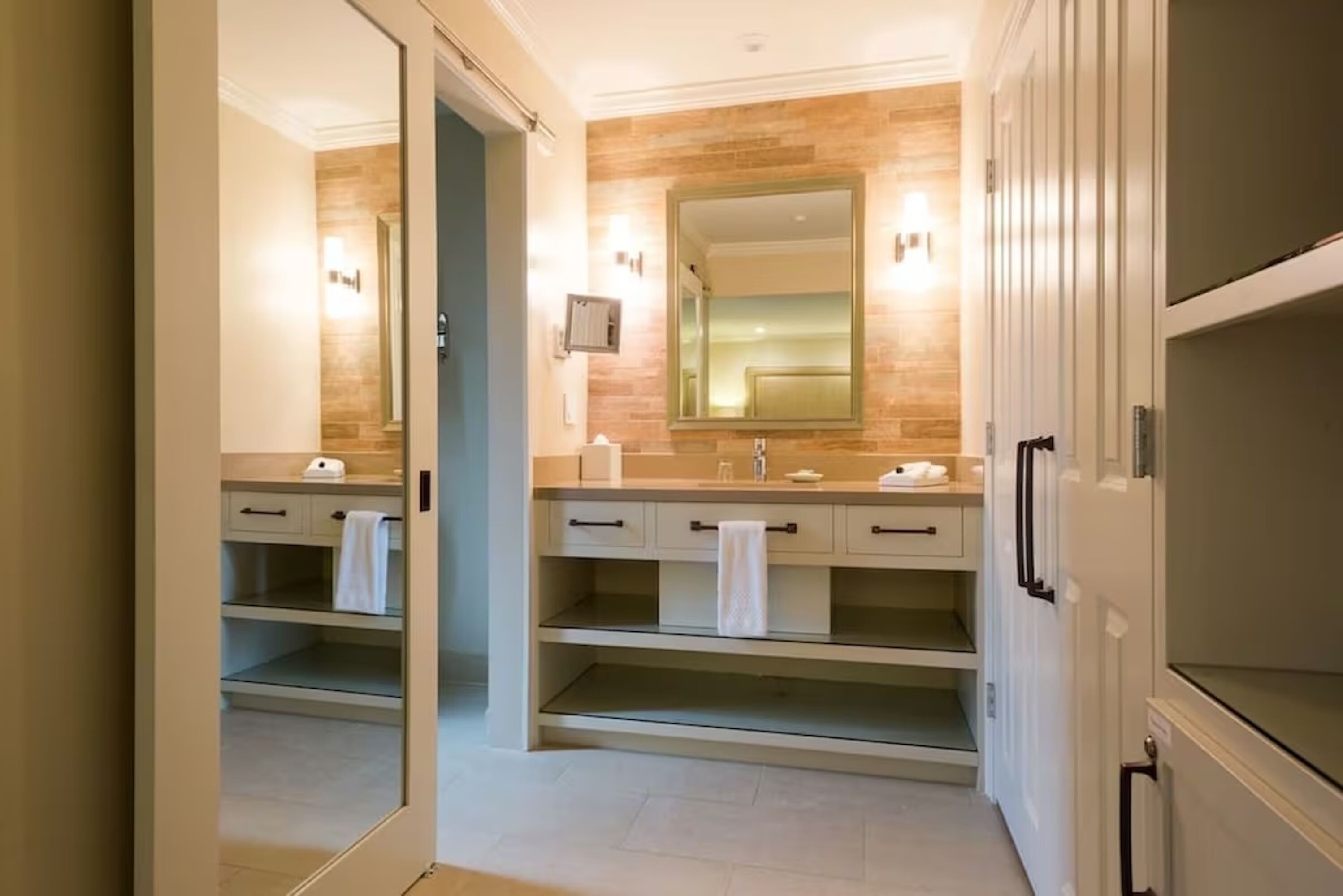 A modern bathroom with a large mirror, two sinks, and a walk-in shower.
