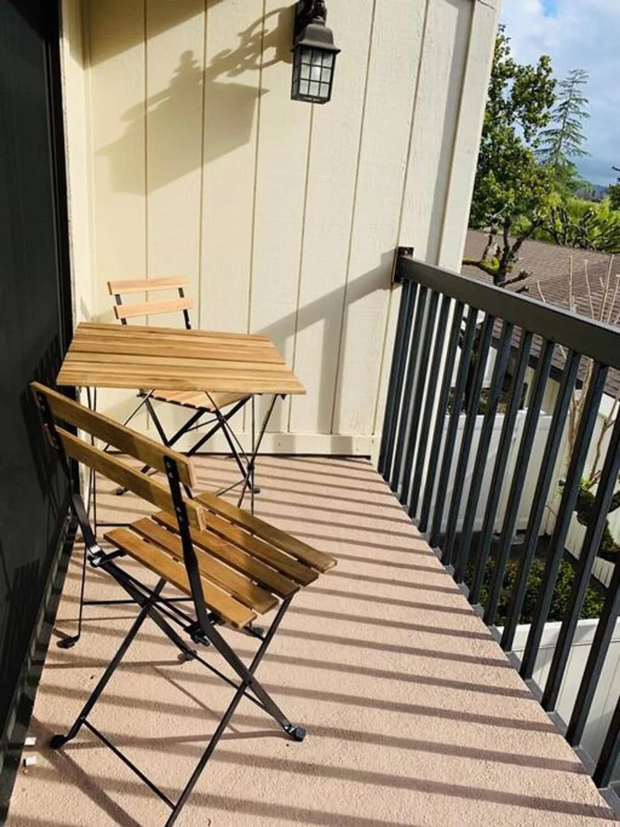 A balcony with a wooden table and chairs, a black railing, and a wall-mounted light fixture.
