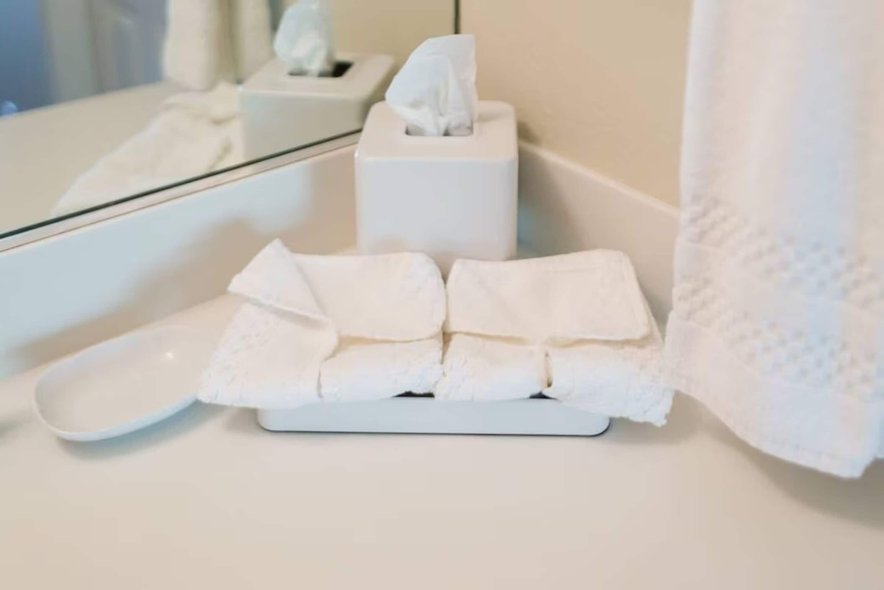 A bathroom with a white sink, a tissue box, and a folded towel on a tray.