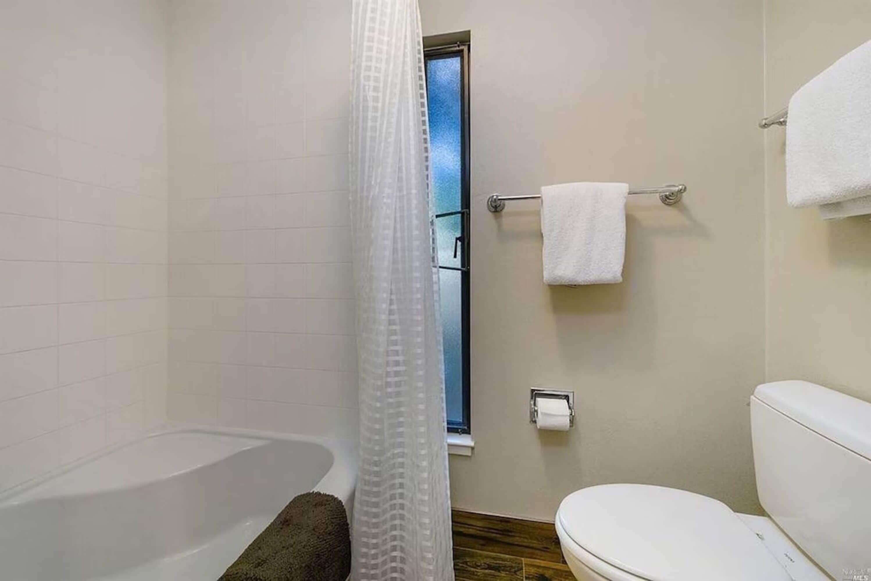 Et badeværelse med badekar, toilet og et vindue.