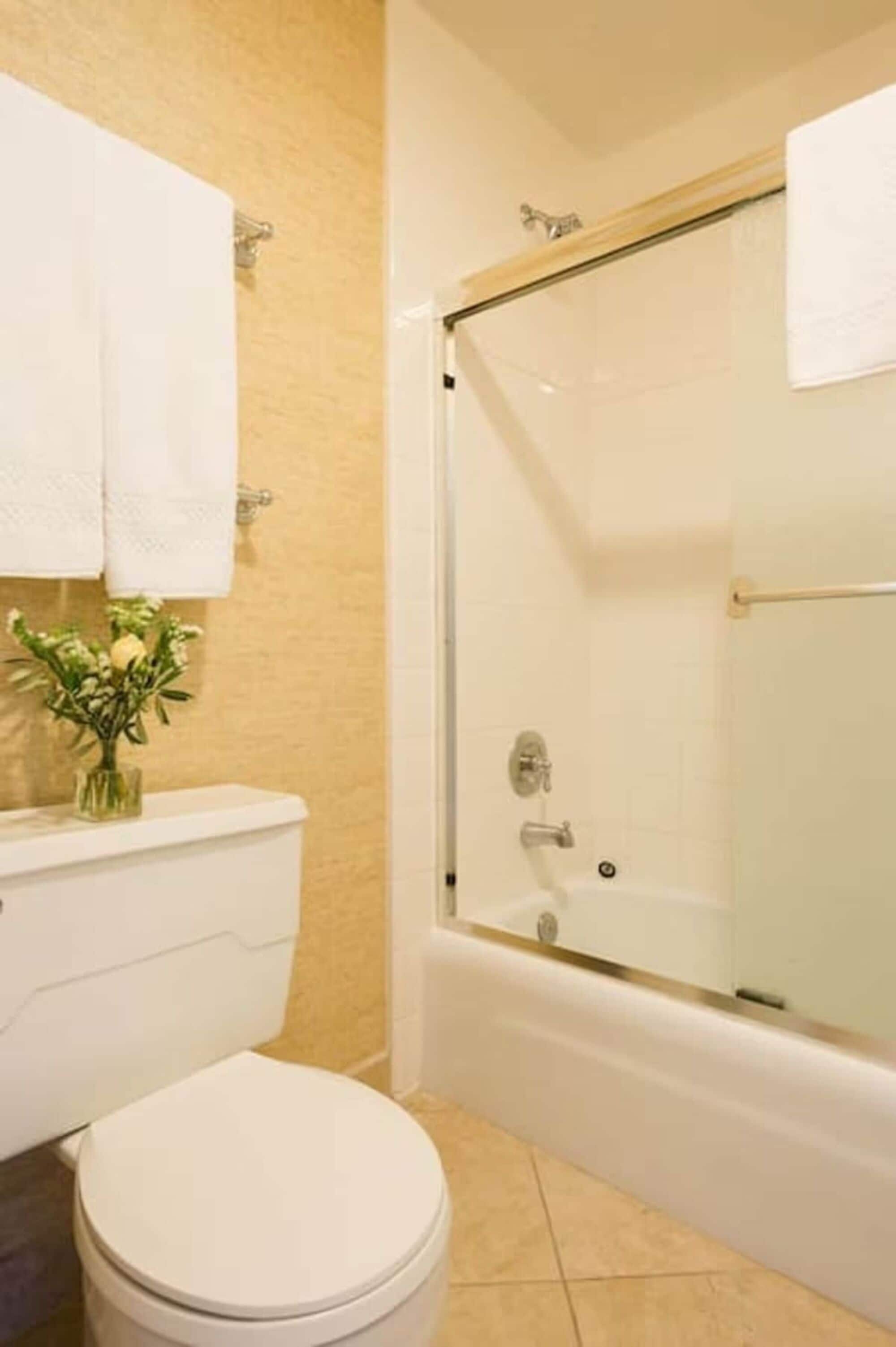 A bathroom with a toilet, a glass-enclosed shower, and a sink with a vase of flowers.