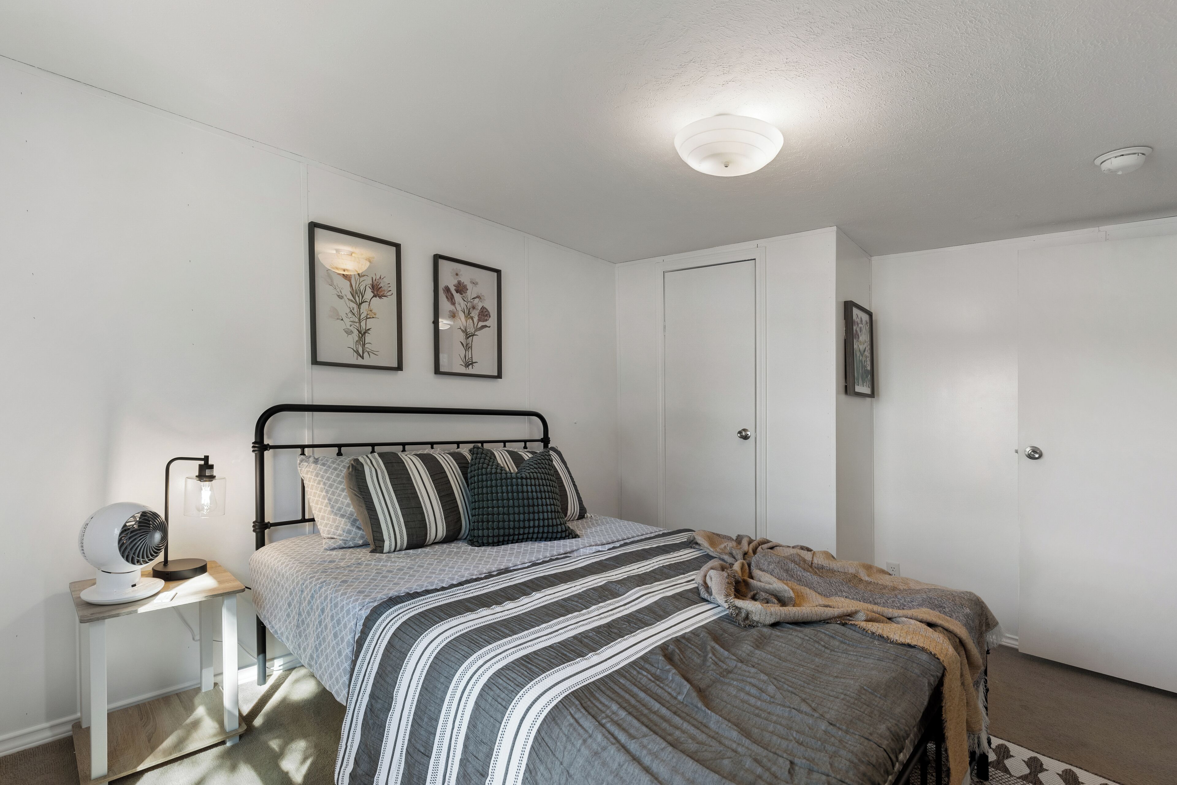 A bedroom with a bed, bedside table, wall-mounted light, and two framed pictures.