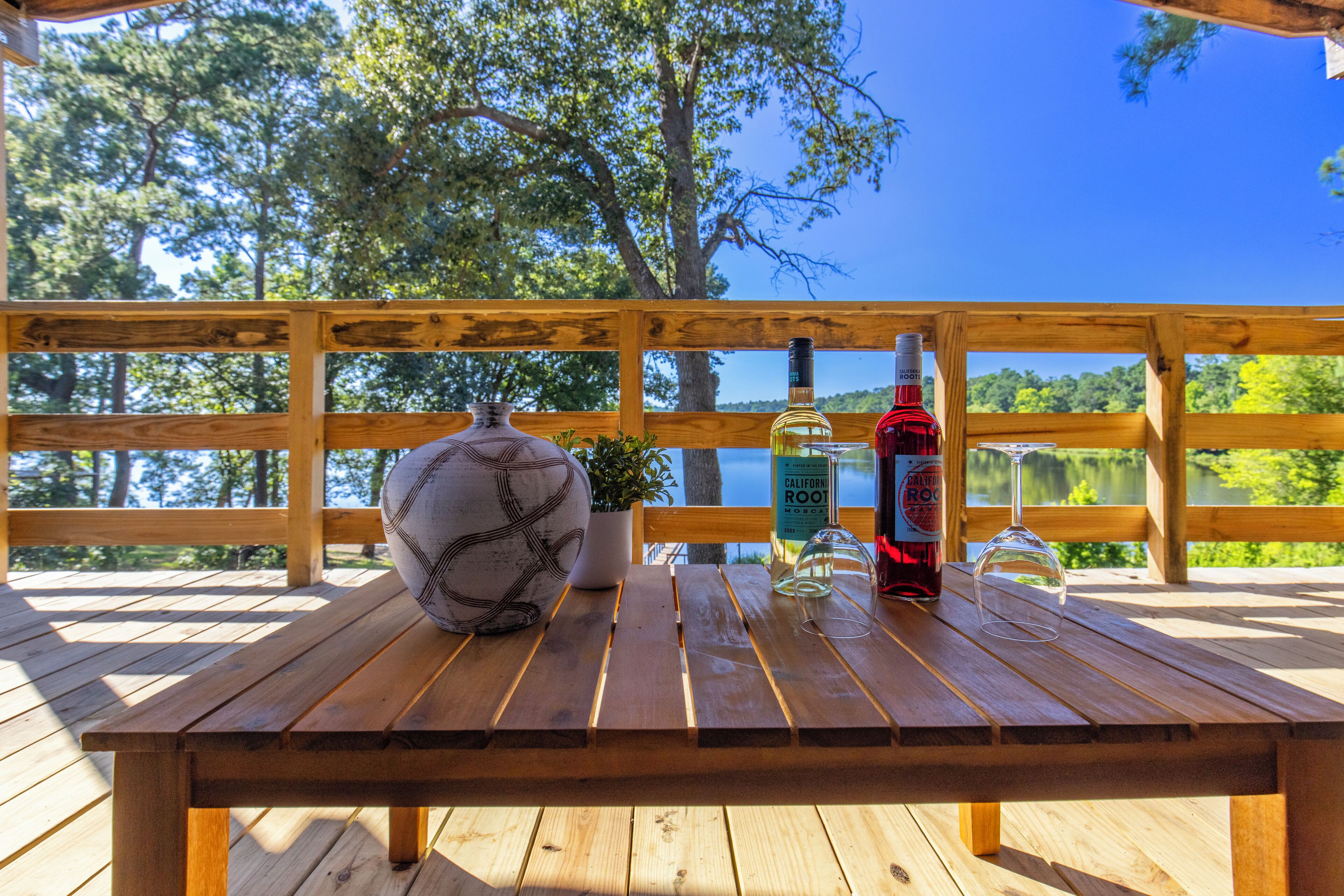 Een houten terras met een tafel, een vaas, een potplant en twee flessen wijn.
