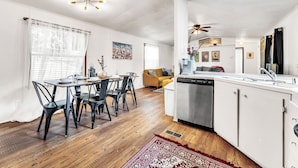 Een moderne keuken met witte kasten, een roestvrijstalen vaatwasser en een eethoek met een houten tafel en zwarte stoelen.