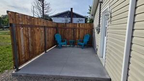 Un patio cubierto con cerca de madera, dos sillas y una mesita.