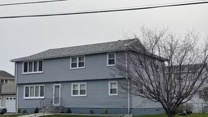 A two-story residential building with a grey exterior, a front porch, and a tree in the front yard. - Spacious 3-Bedroom Home Awaits 2nd Floor - Designed for Comfort & Relaxation!!! (New Britain)