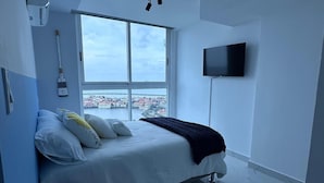 A modern bedroom with a bed, a TV, and a window with a city view.