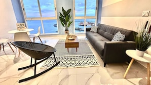 A modern living room with a large window overlooking a body of water, a sofa, a coffee table, and a rocking chair.