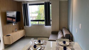 A modern living room with a TV mounted on the wall, a dining area with a table set for two, and a seating area with a sofa. - Edifício Tours Du Porto (Ipojuca)