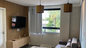 A modern kitchen with a flat-screen TV, wooden panel wall, and a dining area with a table and chairs. - Edifício Tours Du Porto (Ipojuca)