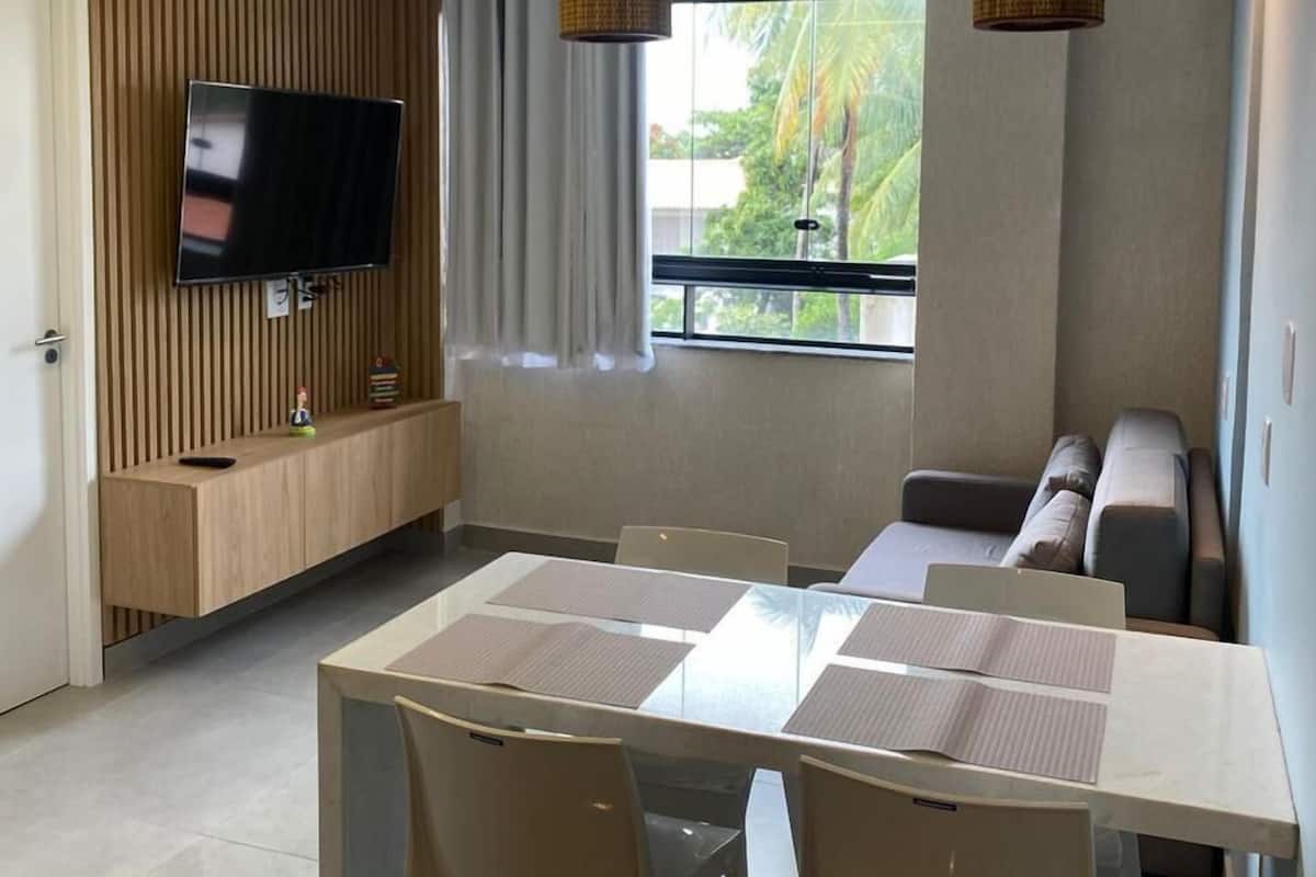 A modern kitchen with a flat-screen TV, wooden panel wall, and a dining area with a table and chairs.