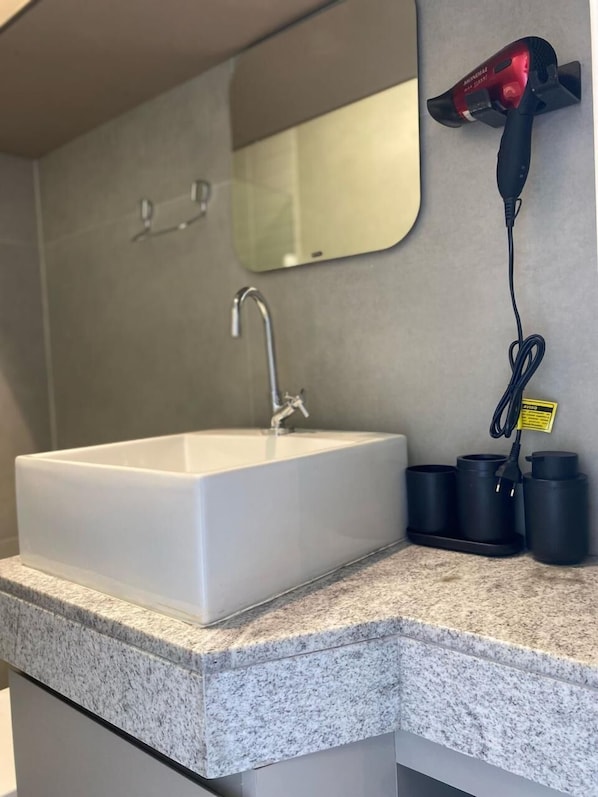 A bathroom with a white sink, a mirror, and a hairdryer on the wall. - Edifício Tours Du Porto (Ipojuca)