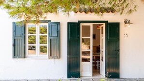 A building with two open doors, one leading to a room with a bed and a table, and the other to a room with a chair and a table.